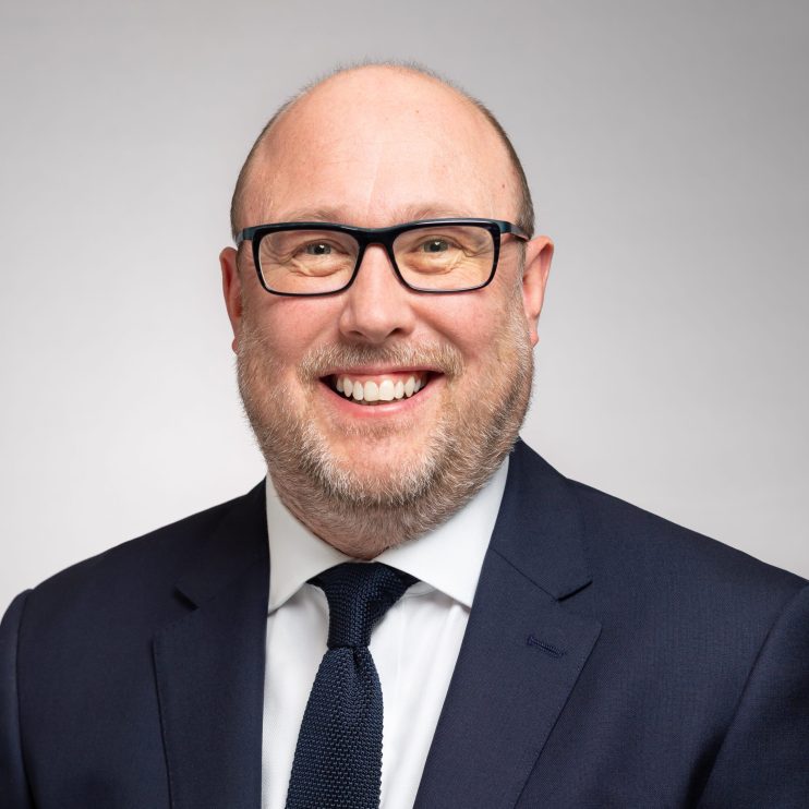 David Bimpson, smiling professional in a navy suit and glasses, white shirt, dark knitted tie