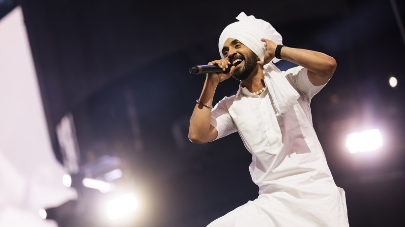 Diljit Dosanjh performing live on stage, wearing a vibrant outfit under bright spotlights.
