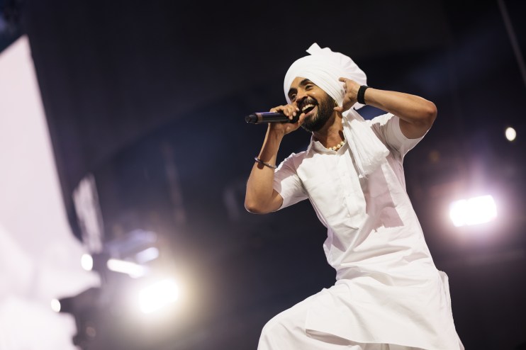 Diljit Dosanjh performing live on stage, wearing a vibrant outfit under bright spotlights.