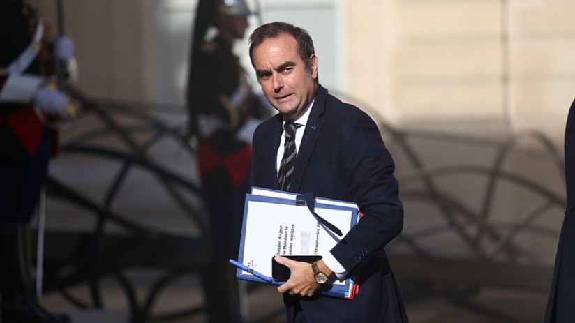 S&eacute;bastien Lecornu, French Prime Minister, carries documents and a phone, with uniformed guards in the background.