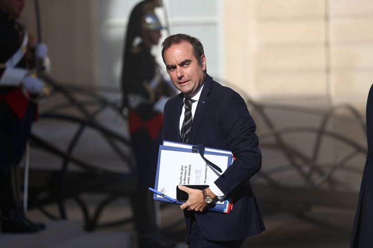 S&eacute;bastien Lecornu, French Prime Minister, carries documents and a phone, with uniformed guards in the background.