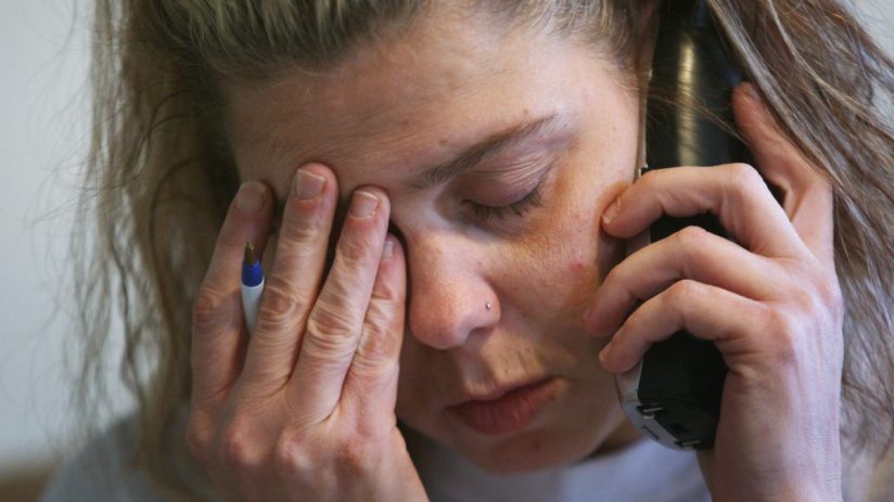 Frustrated woman holding phone to ear, rubbing eyes, possibly stressed by a call.