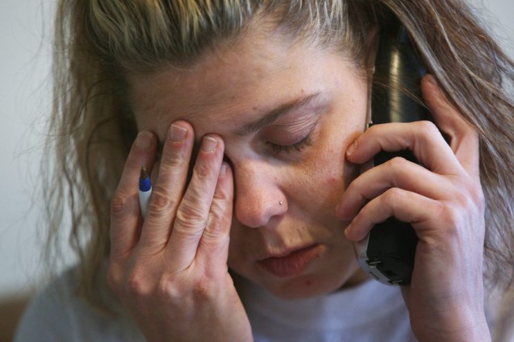 Frustrated woman holding phone to ear, rubbing eyes, possibly stressed by a call.