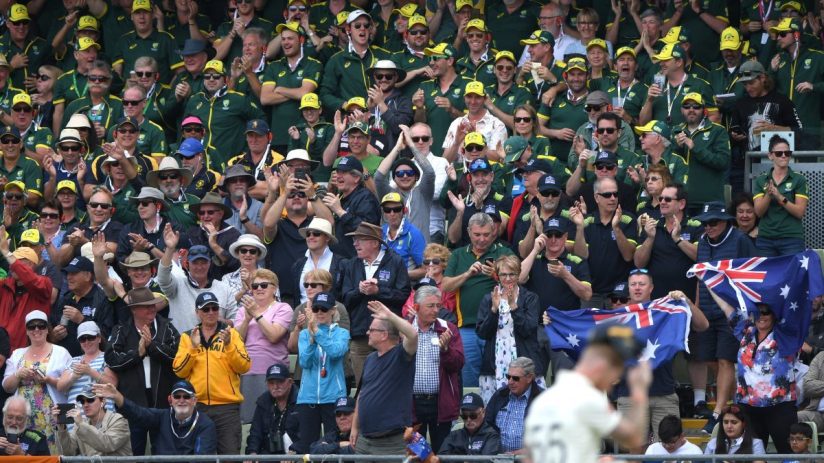 Crowd of Australian cricket fans cheering, many wearing green and gold uniforms and hats, some holding flags.