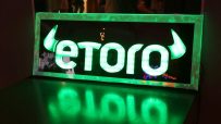 eToro logo in bright green neon light, reflecting on a dark, glossy surface.