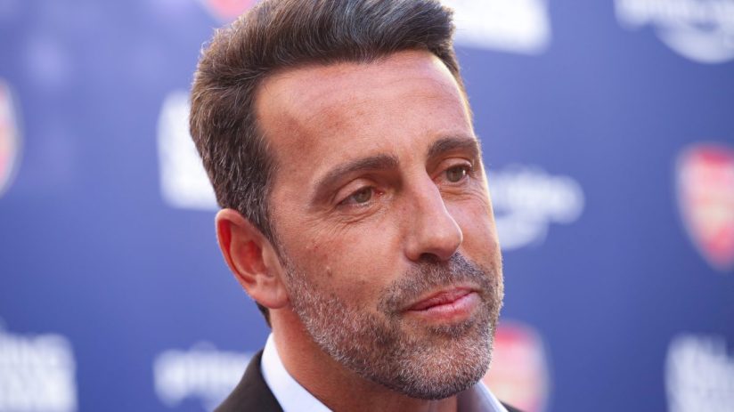 Close-up of a man with salt-and-pepper hair and beard, wearing a suit, against a blurred blue background.