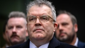 Tom Watson, former Labour MP, wearing glasses, a dark coat, and a tie, looking seriously forward.
