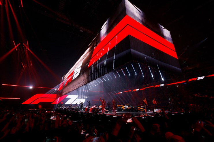 Formula 1 75th anniversary celebration event with F1 cars and drivers on stage, surrounded by red lights and a crowd