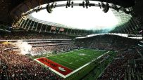 Packed stadium during an American football game, showing the field, a large crowd, and flags.