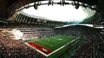 Packed stadium during an American football game, showing the field, a large crowd, and flags.