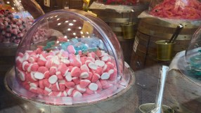 Bulk display of pink and white gummy candies in a clear dome on a wooden barrel in a candy store