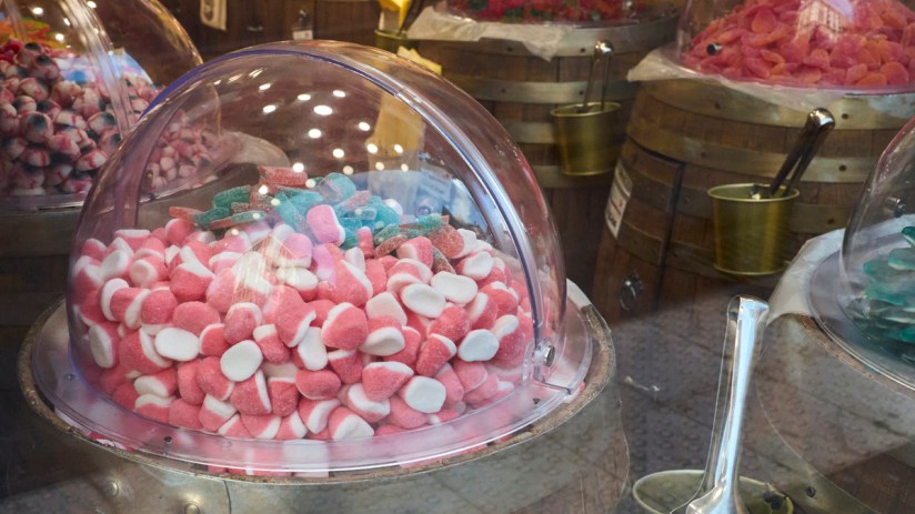 Bulk display of pink and white gummy candies in a clear dome on a wooden barrel in a candy store