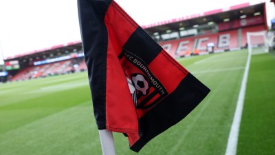 AFC Bournemouth corner flag with team logo, vibrant green pitch, and stadium seating in the background.