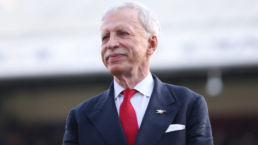 Stan Kroenke, Arsenal Football Club owner, smiling in a navy suit with a red tie and Arsenal pin.