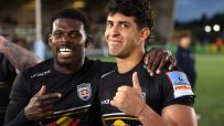 Two rugby players in black Newcastle Falcons jerseys, one pointing and the other giving a thumbs-up, smiling after a game.