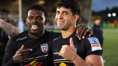 Two rugby players in black Newcastle Falcons jerseys, one pointing and the other giving a thumbs-up, smiling after a game.