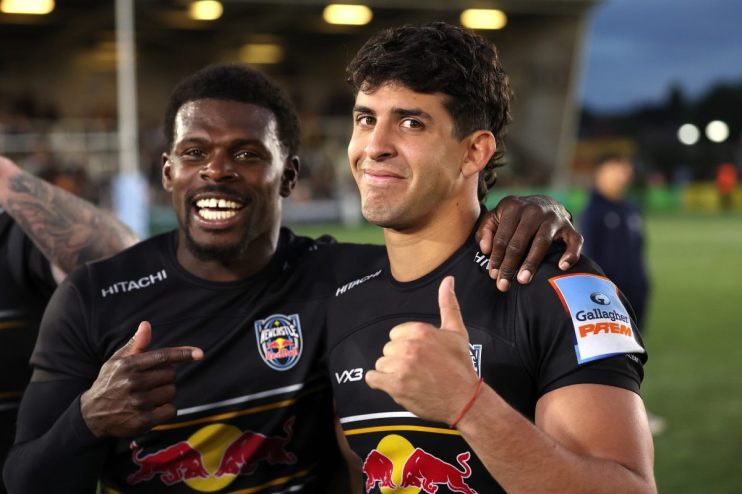 Two rugby players in black Newcastle Falcons jerseys, one pointing and the other giving a thumbs-up, smiling after a game.