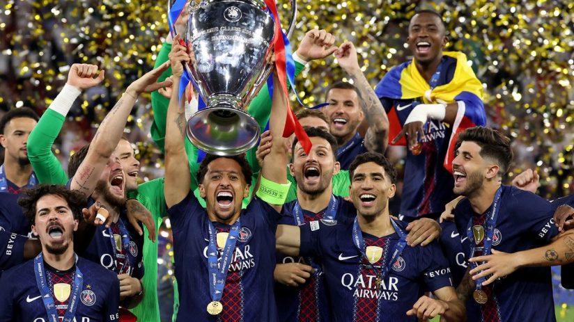 PSG players celebrate with the UEFA Champions League trophy and gold medals as confetti falls.