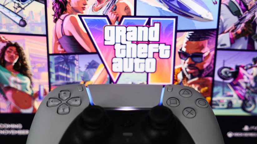 PlayStation 5 controller in front of a screen displaying the Grand Theft Auto logo and game art