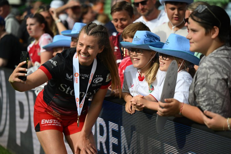 Female rugby player with medal takes selfie with young fans in blue hats at a stadium event