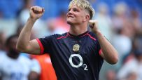 Rugby player in a dark blue jersey with a red trim and O2 logo, raising clenched fists in celebration.