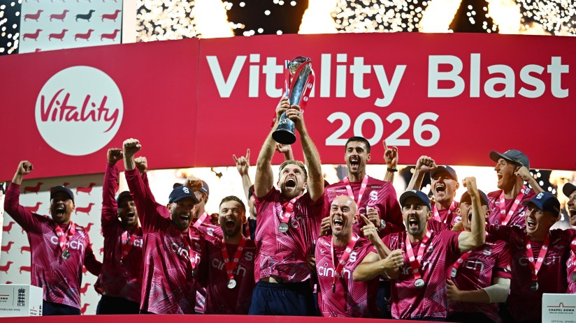 Cricket team in pink jerseys celebrating a Vitality Blast 2026 championship win, holding up the trophy with fireworks.