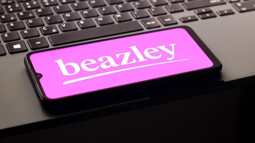 A smartphone displaying the white Beazley logo on a bright pink screen, resting on a dark laptop keyboard.