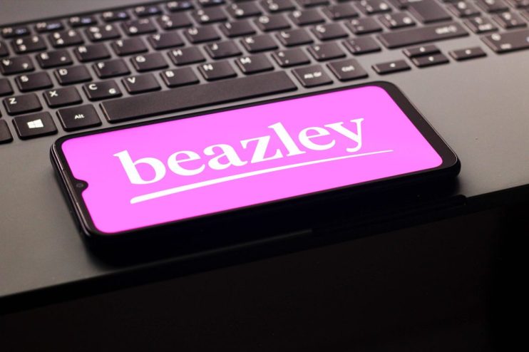 A smartphone displaying the white Beazley logo on a bright pink screen, resting on a dark laptop keyboard.