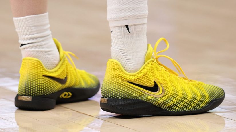 Close-up of a persons feet wearing bright yellow and black Nike basketball shoes with white socks on a wooden court