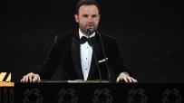 Juan Mata speaking at a podium with microphones, wearing a black velvet tuxedo and bow tie.