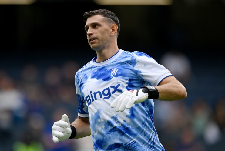 Emiliano Martínez in a blue and white tie-dye Aston Villa goalkeeper kit with BingX sponsor logo and white gloves.