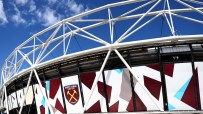 Exterior of London Stadium (formerly Olympic Stadium) with West Ham United logo against a blue sky