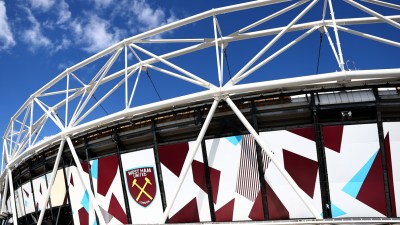 Exterior of London Stadium (formerly Olympic Stadium) with West Ham United logo against a blue sky