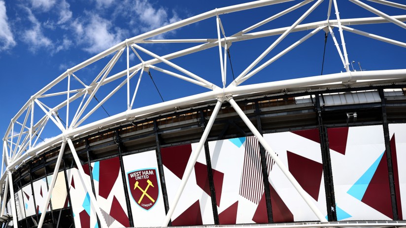 Exterior of London Stadium (formerly Olympic Stadium) with West Ham United logo against a blue sky