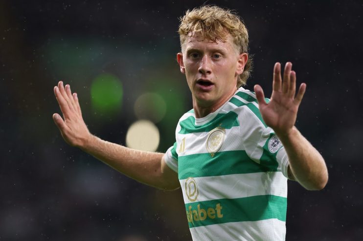 Blonde male football player in green and white striped Celtic jersey raising hands on field