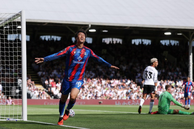 Footballer in red and blue jersey celebrating a goal with arms outstretched on a sunny field