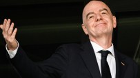 Gianni Infantino, FIFA President, in a dark suit and tie, smiling and raising his hand.