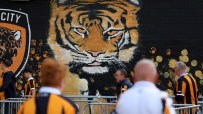 Large tiger mural on a black wall with orange handprints and fans in striped shirts walking by.