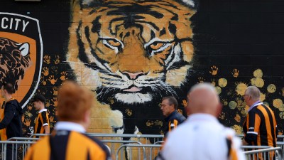 Large tiger mural on a black wall with orange handprints and fans in striped shirts walking by.