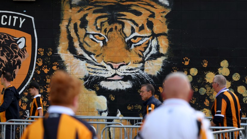 Large tiger mural on a black wall with orange handprints and fans in striped shirts walking by.