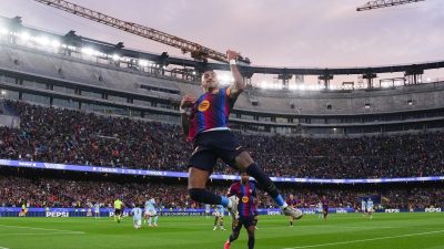 FC Barcelona player Raphinha celebrates a goal in a packed stadium during a UEFA Champions League match.