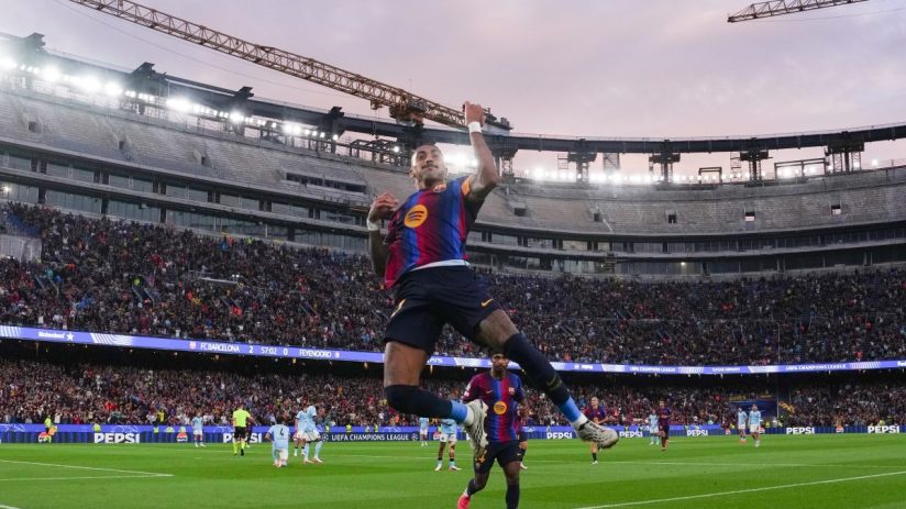 FC Barcelona player Raphinha celebrates a goal in a packed stadium during a UEFA Champions League match.