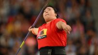 Female javelin thrower in red top and black waist support, mid-throw with intense focus at a sports event.