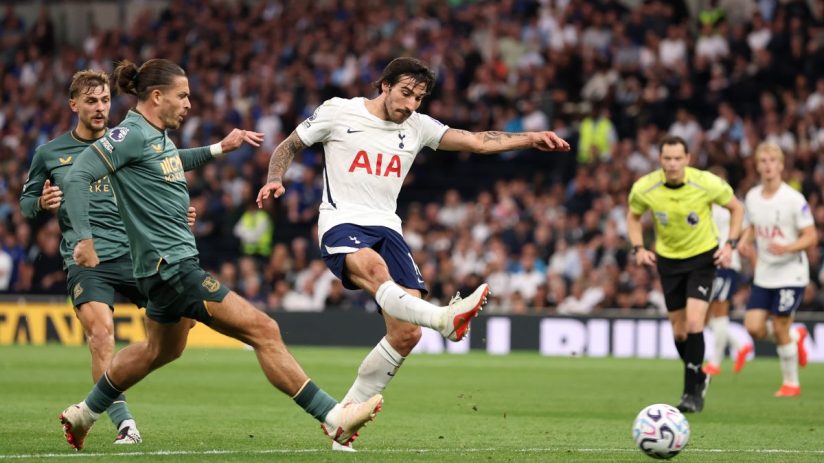 Tottenham player kicking a soccer ball during a match, opponent defender near, referee in background