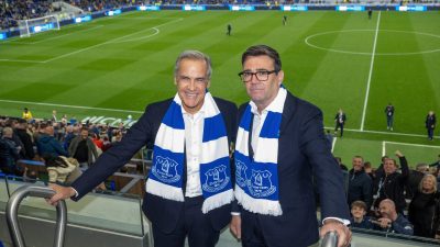 Two men in suits and Everton FC scarves smiling at a football stadium.