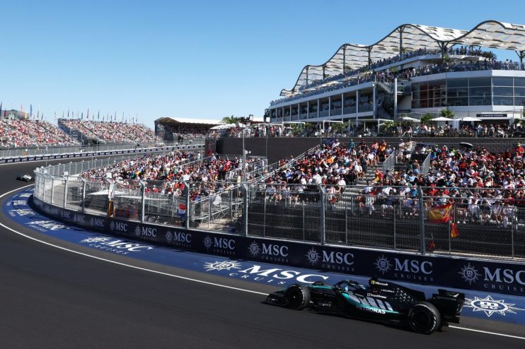 Formula 1 race car on track with fans in grandstands and luxury boxes under a sunny sky