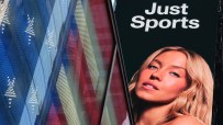 Large digital billboard for Just Sports featuring a woman with blonde hair, next to a reflective building.