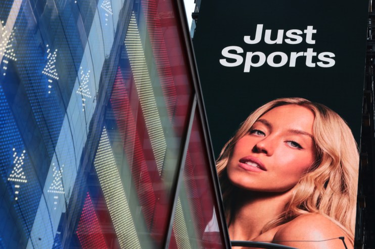 Large digital billboard for Just Sports featuring a woman with blonde hair, next to a reflective building.