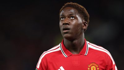 Young male football player in a red Manchester United jersey, looking up with sweat on his face.