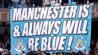 A large banner reads Manchester Is & Always Will Be Blue! with Manchester City F.C. crests, surrounded by cheering fans.
